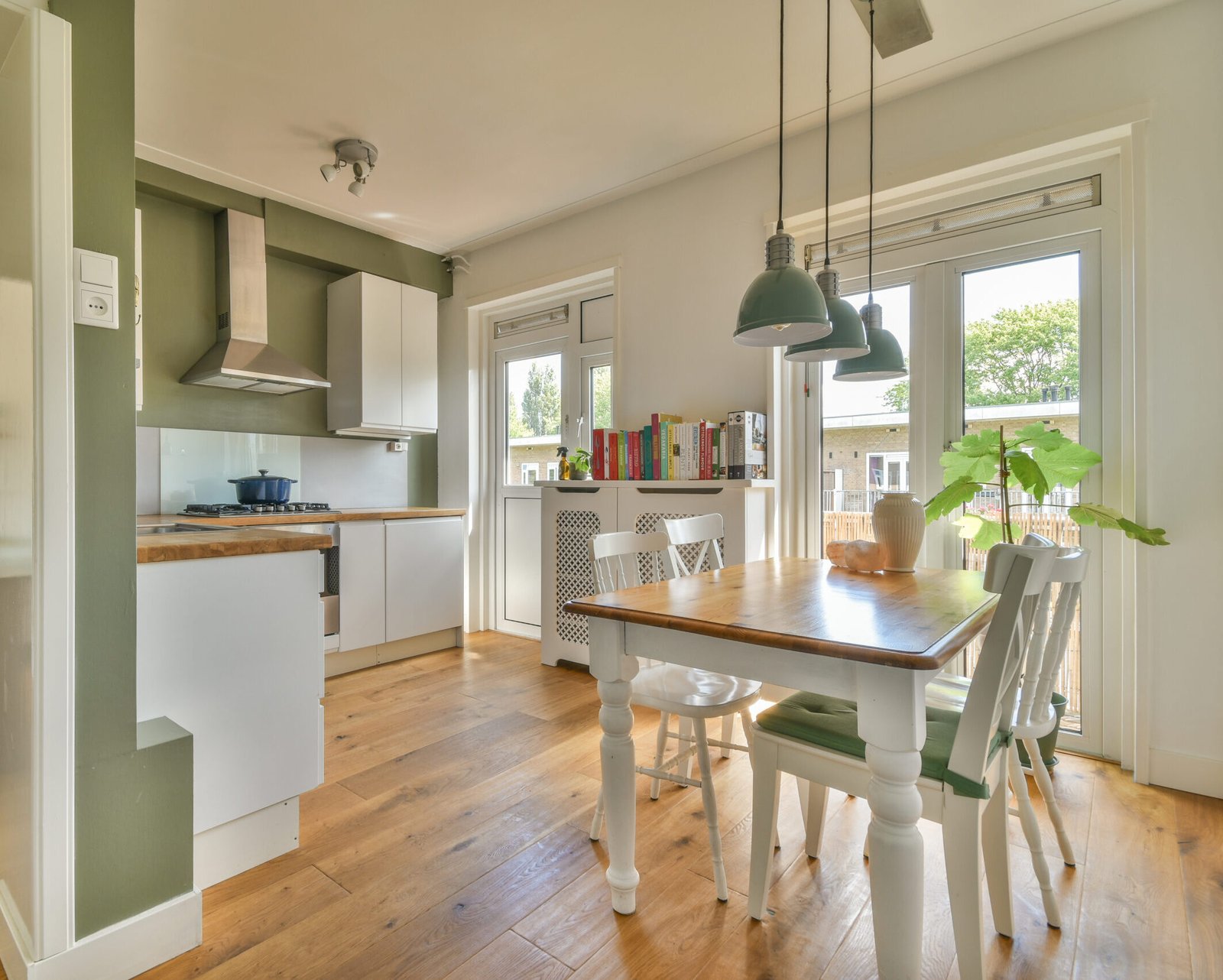 a kitchen and dining area in a house with wood floors, white cabinets, green walls and an open door leading to the patio
